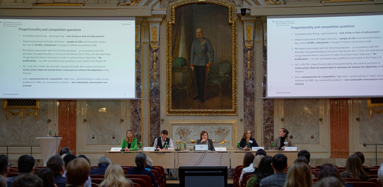 Podium des LIDC 2025 in Wien mit fünf Personen vor Publikum, zwei Leinwänden mit Präsentationstext und großem Porträt im Hintergrund.