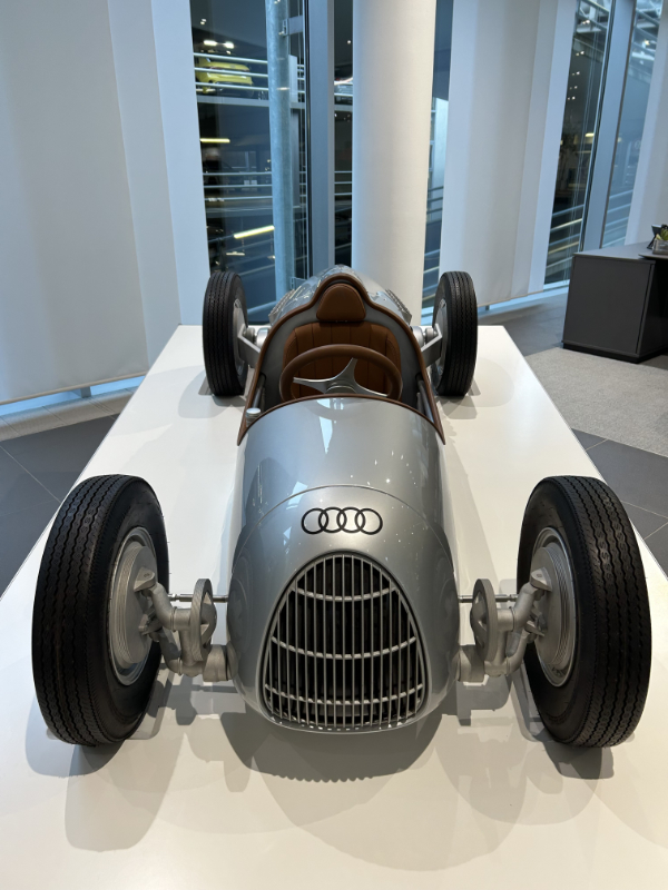 Frontansicht eines historischen Auto Union 'Silberpfeil' Rennwagens in klassischem Silber mit markantem Kühlergrill und braunem Ledersitz im Audi Forum.