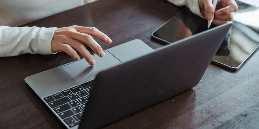 Eine Person bedient auf einem dunklen Holztisch einen Laptop mit einer Hand, während die andere Hand einen Tablet-Stift über einem Tablet hält.