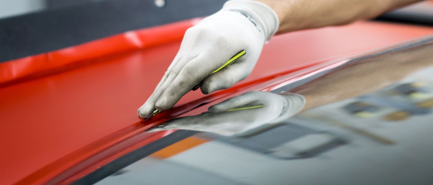 Hand in weißem Handschuh hält Cuttermesser, während sie eine rote Folie auf glatter Oberfläche befestigt