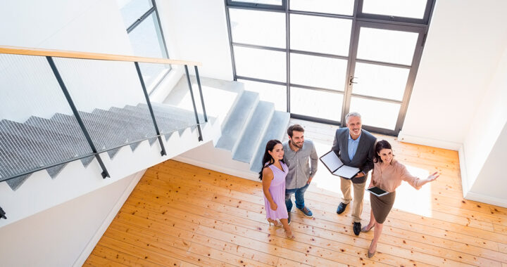 Immobilienmakler zeigen einem Paar ein neues Haus; sie stehen im hohen, lichtdurchfluteten Eingangsbereich.