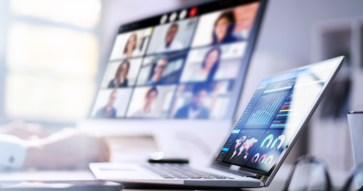 Laptop mit Statistiken, Person legt Hand auf Schreibtisch, im Hintergrund ist Bildschirm mit Videokonferenz zu erahnen.