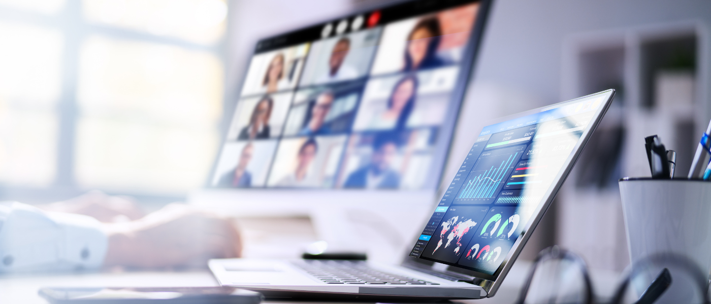 Laptop mit Statistiken, Person legt Hand auf Schreibtisch, im Hintergrund ist Bildschirm mit Videokonferenz zu erahnen.