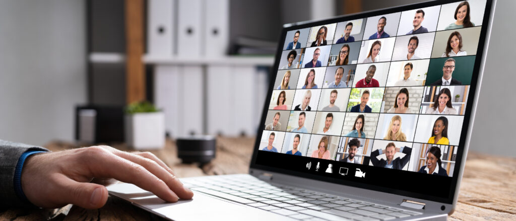 Laptop, auf dem ein Videokonferenzbildschirm mit vielen kleinen Teilnehmerkacheln angezeigt wird.