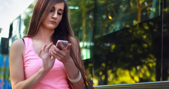 Eine Dame steht vor einem Bus, die auf ihr Handy schaut und darauf tippt.