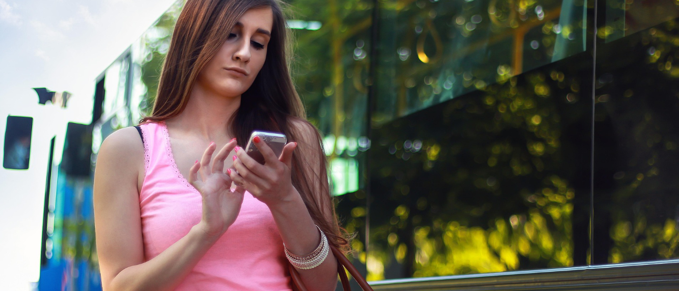 Eine Dame steht vor einem Bus, die auf ihr Handy schaut und darauf tippt.