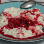 Milchreis auf blauem Teller mit Kirschen und Beeren und einem Löffel am Tellerrand.