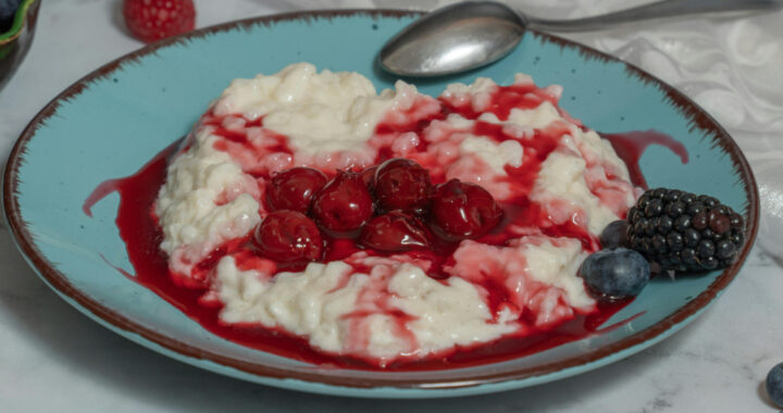 Milchreis auf blauem Teller mit Kirschen und Beeren und einem Löffel am Tellerrand.