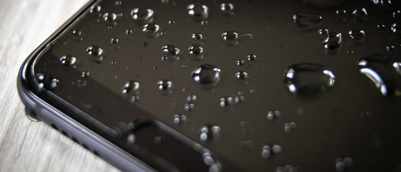 Nahaufnahme eines Ausschnitts eines schwarzen Smartphones mit mehreren Wassertropfen auf dem Bildschirm.