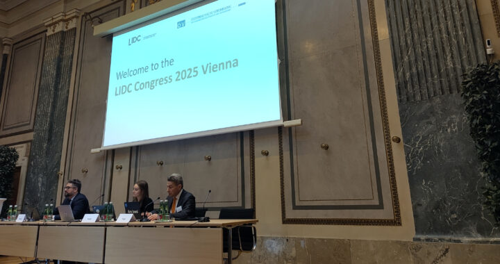 Podium mit drei Personen, in ihrem Hintergrund eine große Leinwand auf der eingeblendet ist 'Welcome to the LIDC Congress 2025 Vienna'.