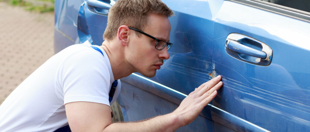 Mechaniker begutachtet Unfallschaden an der Seite eines blauen Autos.