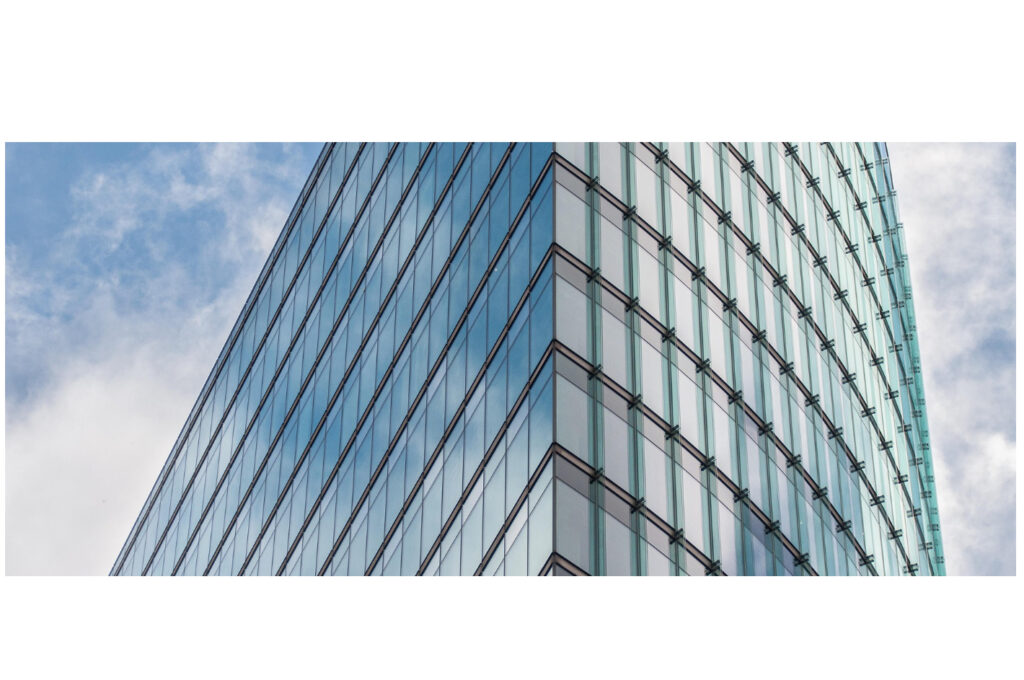 Moderne Glasfassade eines Hochhauses mit spiegelnden Fenstern und abgerundeter Ecke vor blauem Himmel.