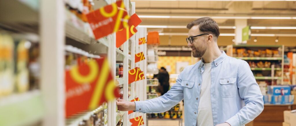 Mann geht durch Supermarkt, am Regal hängen Prozentschilder