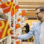 Mann geht durch Supermarkt, am Regal hängen Prozentschilder