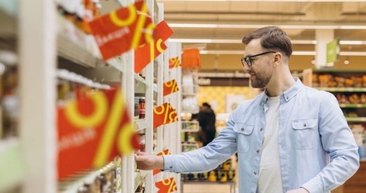 Mann geht durch Supermarkt, am Regal hängen Prozentschilder