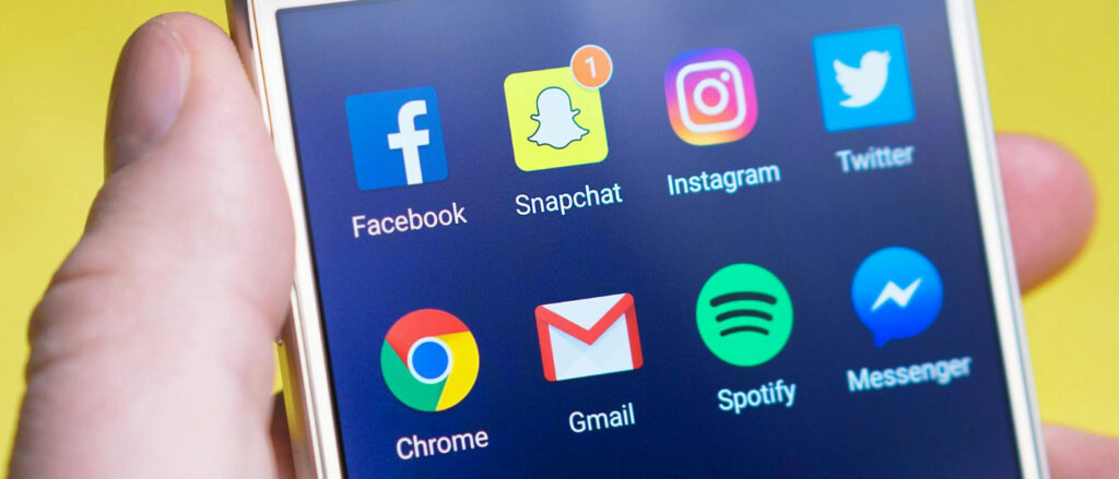 Smartphone-Bildschirm mit den App-Symbolen von Facebook, Snapchat (mit Benachrichtigung), Instagram, Twitter, Chrome, Gmail, Spotify und Messenger.