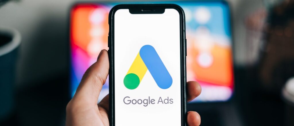 Hand mit Smartphone in der Hand, auf dem Google Ads Logo zu sehen ist