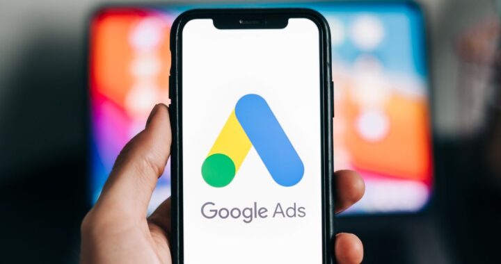 Hand mit Smartphone in der Hand, auf dem Google Ads Logo zu sehen ist