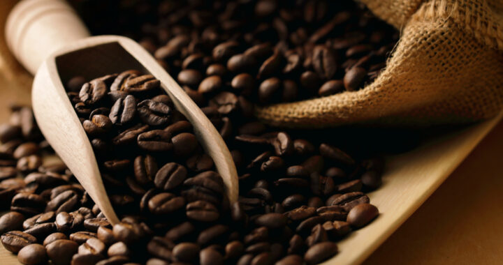 Zu sehen sind Kaffeebohnen, die aus einem Jutesack kommen. Ein Teil der Bohnen liegt in einer Holzkelle.