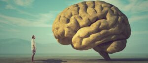 In einer surrealen Darstellung im Retro-Stil steht ein kleiner Mann vor einem riesengroßen Gehirn aus Stein in einer weiten, surrealen Landschaft.