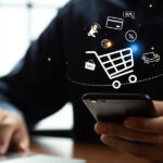 Eine Person tippt auf einem Smartphone; darüber schwebt eine digitale Grafik eines Einkaufswagens mit verschiedenen Symbolen, die Online-Shopping visualisieren.