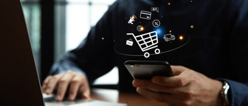 Eine Person tippt auf einem Smartphone; darüber schwebt eine digitale Grafik eines Einkaufswagens mit verschiedenen Symbolen, die Online-Shopping visualisieren.