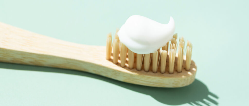 Holzzahnbuerste mit Zahnpasta vor grünem Hintergrund.