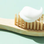 Holzzahnbuerste mit Zahnpasta vor grünem Hintergrund.