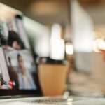 Bild eines Webinars, Person schaut in Laptop, auf dem sprechende Personen abgebildet sind