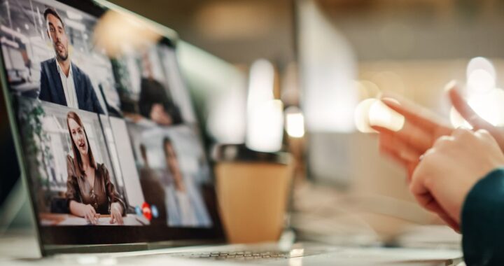 Bild eines Webinars, Person schaut in Laptop, auf dem sprechende Personen abgebildet sind