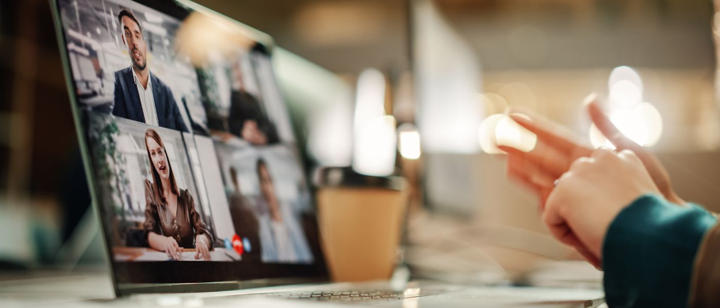 Bild eines Webinars, Person schaut in Laptop, auf dem sprechende Personen abgebildet sind