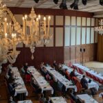 Blick von oben auf Tagung mit Person, die Rede hält und zahlreichen Personen, die zuhören