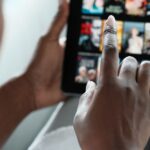 Finger zeigt auf Tablet, das zahlreiche Streamingtitel zur Auswahl anzeigt