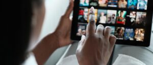 Finger zeigt auf Tablet, das zahlreiche Streamingtitel zur Auswahl anzeigt