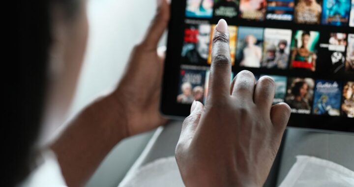 Finger zeigt auf Tablet, das zahlreiche Streamingtitel zur Auswahl anzeigt