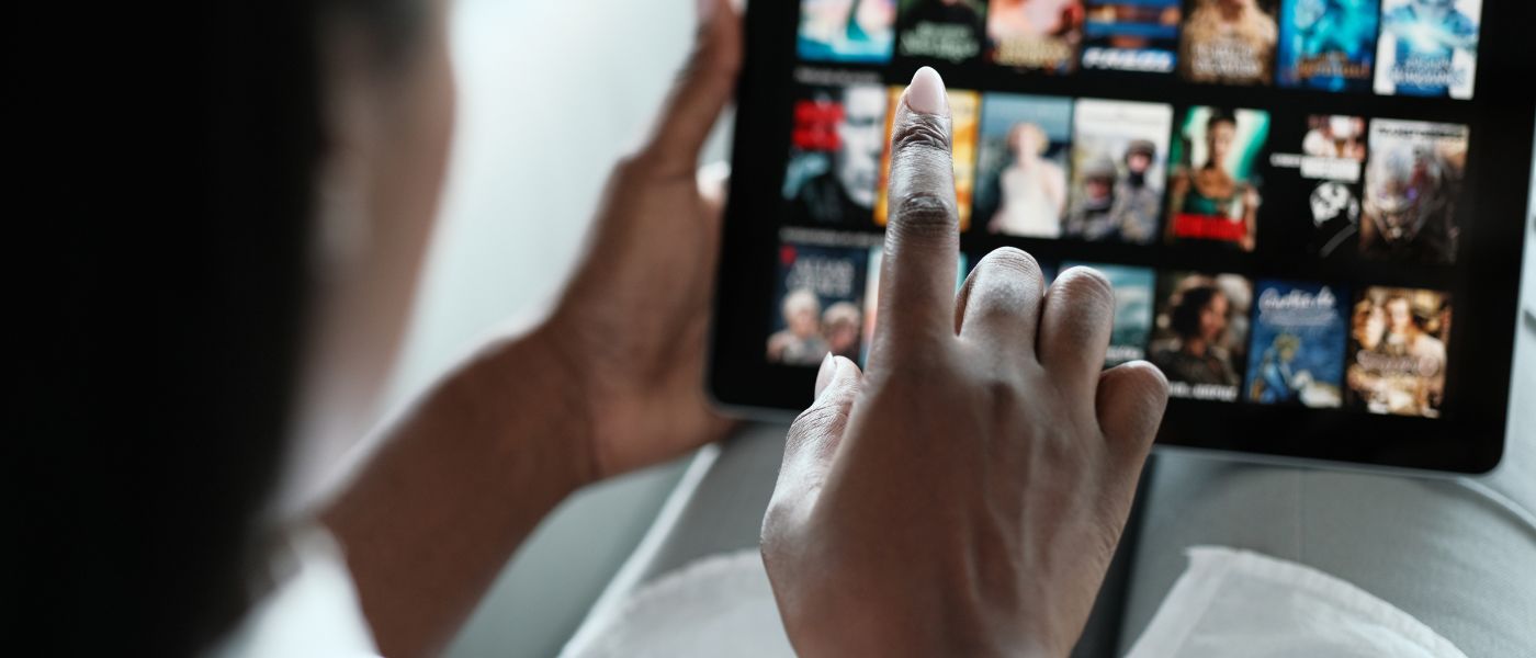 Finger zeigt auf Tablet, das zahlreiche Streamingtitel zur Auswahl anzeigt